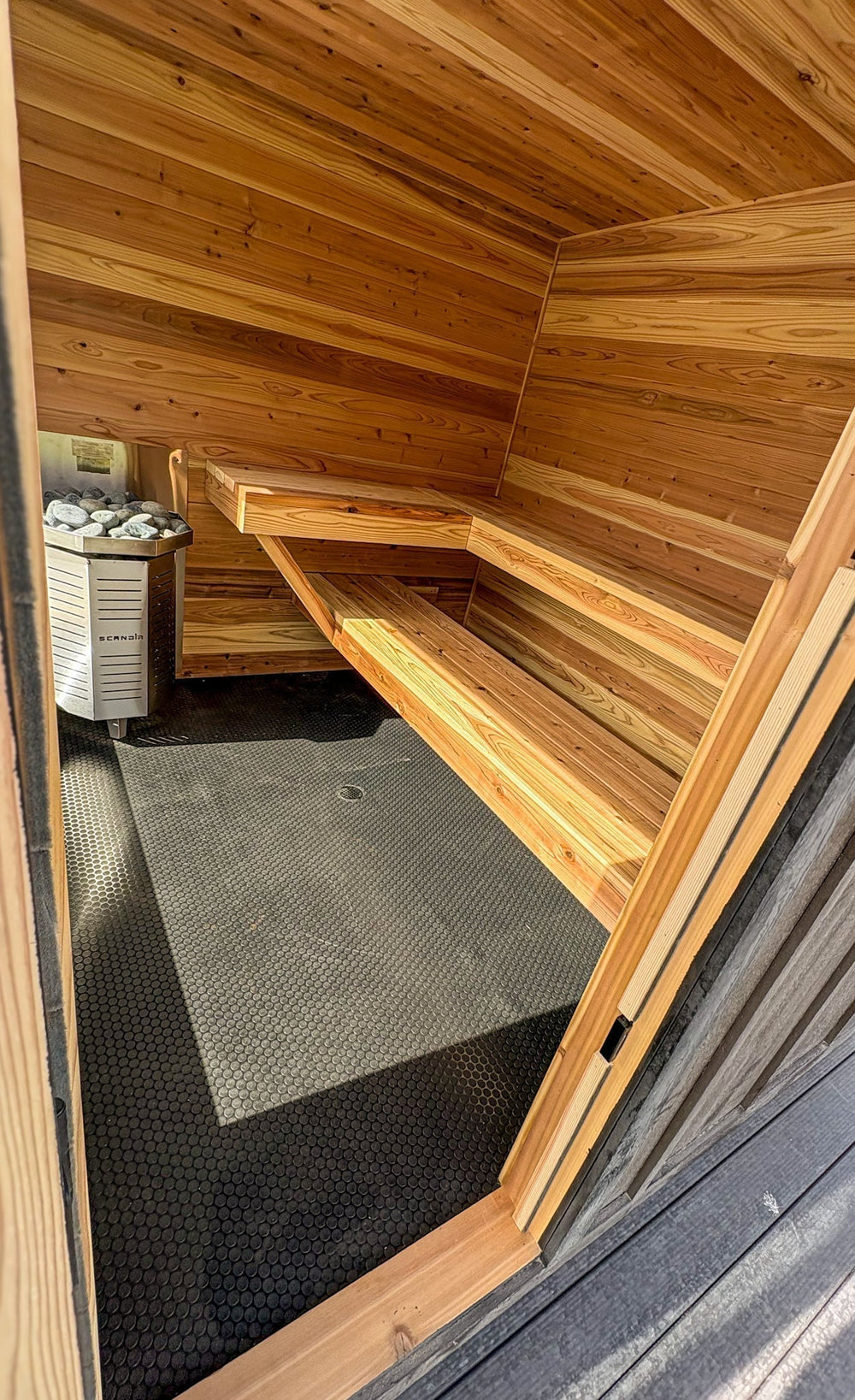 Interior of a Blazin Saunas cedar sauna in eastern Idaho showing the heater and stones beside two-level cedar benches